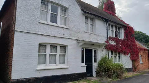 BBC/ALAN WEBBER A white-painted brick-built pub, with a black door and five windows. The leaves of a red climbing plant cover one end of the building.