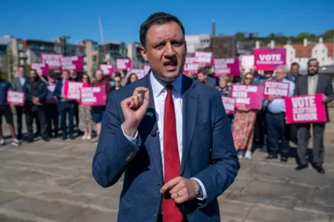 PA Media Anas Sarwar, mid speech with his fingers gesturing. He is standing in front of a crowd of people wearing a navy suit and red tie.