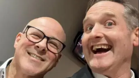 Jim Thompson Two men smiling to camera. On the left is Kyle Jaggers, a bald man with black rimmed glasses. On the right is Jim Thompson, who is also smiling. He has greying hair and is wearing a grey suit and white shirt. 