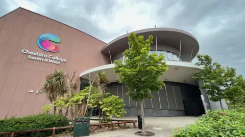 A college building with a rounded entrance and trees in front of it. There is signage on the side of the building which identifies it as Cheshire College South and West.