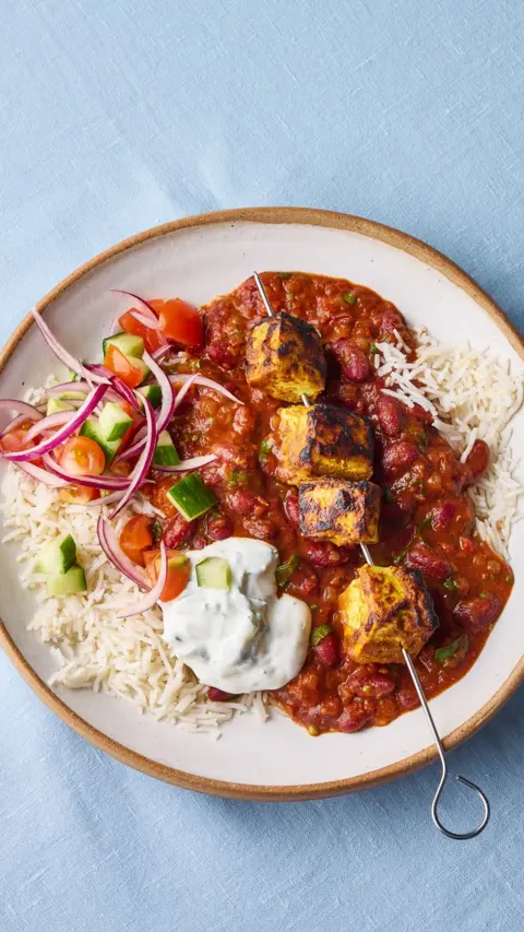 Top-down view of a plate with a tofu skewer sitting a bed of curry and rice