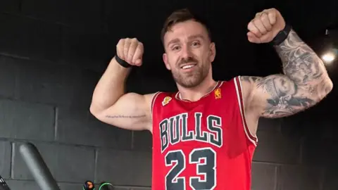 Luke flexes his muscles on the stairclimbing machine and smiles ahead of his challenge.