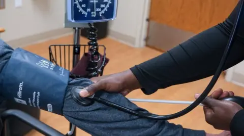 A nurse takes a patient's blood pressure, applying a stethoscope to their arm as they wear a blood pressure armband.