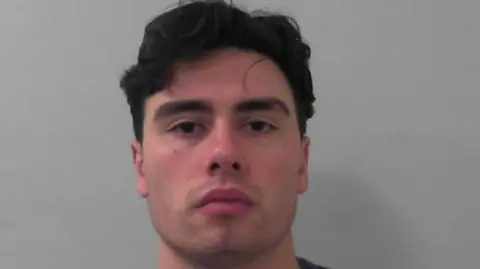 Mckenzie Dicicco with thick black hair, stubble and looking serious in his mugshot.