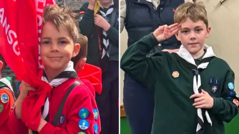 Two photos side-by-side showing brothers Finley and Tobias Rice. Finley is wearing a red scouts uniform with badges down the arm and is hugging a red flag on a pole. Finley is wearing a green scouts uniform and is making the three-finger scouts salute. Both boys have short fair hair.