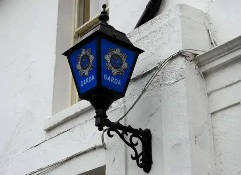 A blue street lap with the Garda crest on it against a white wall