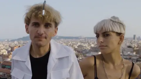 First Born Films Neil Harbisson em uma camisa branca e Moon Ribas em um colete preto, em um telhado de Barcelona