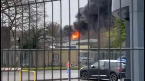 Ben Meighan-Carey Black smoke billows from an orange glow of the fire with several cars in the foreground