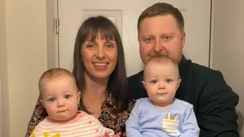 Rachel Williams Rachel Williams and her family, including her partner and two young twins, smile into the camera.