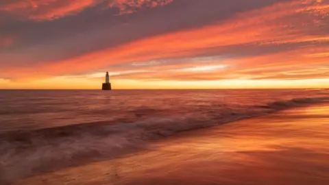 Fabio Todde A beach at sunrise with a  lighthouse in the background