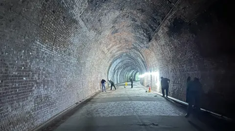 A long brick tunnel with people in the distance sweeping the ground. 