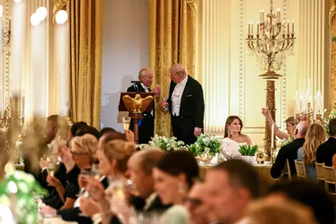AFP via Getty Images The King and president cheers champagne glasses while Melania looks on, with guests in the foreground, at the state banquet.