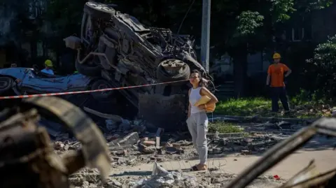 A woman looks at destroyed vehicles at the site of a damaged school which was hit during Russian drone and missile strikes