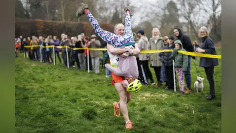 PA A man runs holding a woman upside down to his chest. 