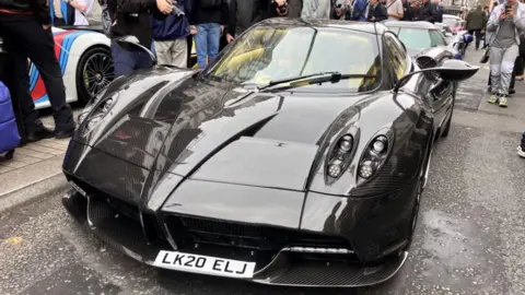 Asad Ahmad/BBC A Pagani Huayra Roadster, a black supercar with antenna-like wing mirrors, parked up on Pall Mall.