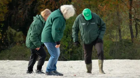 ZSL Three people wearing dark green jackets are looking at the chalky ground as they stomp on it