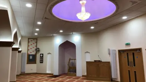 Contributed Inside a mosque with a purple dome in the ceiling and patterned prayer mats on the carpet. 