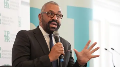 PA Media James Cleverly holding a microphone at a think tank event