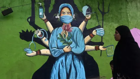 Getty Images A Muslim woman is walking past a mural painting of a face wearing masks amid a sudden surge of the JN.1 coronavirus in Mumbai, India, on January 11, 2024.