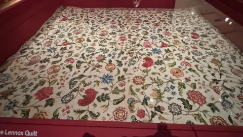 A quilt on display. It has floral designs. 