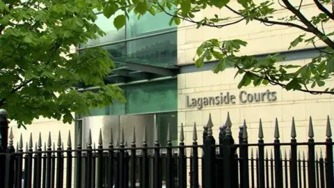 BBC Outside of Laganside Courts, Belfast. A black wrought-iron fence stands in front of the building, which is constructed from portland stone.