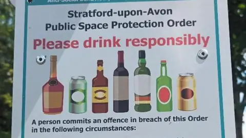 A white sign with red and black text reading Please drink responsibly , images of varying size bottles and cans are also shown.