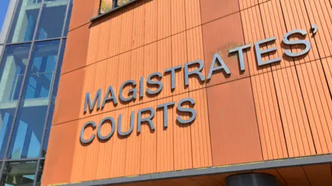 Lewis Adams/BBC The orange magistrates' court building, which has silver lettering on it that says "Magistrates' courts". It has a glass entrance and stairs are visible through glass to the left