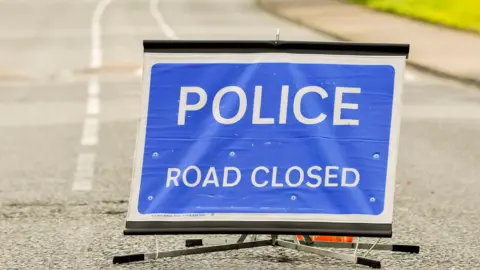 A blue police signs stating that the road is closed.