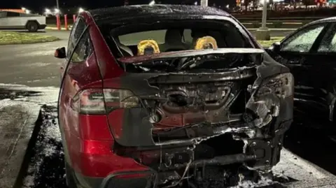 US Justice Department The back end of a burnt-out red car pictured at night in a parking lot