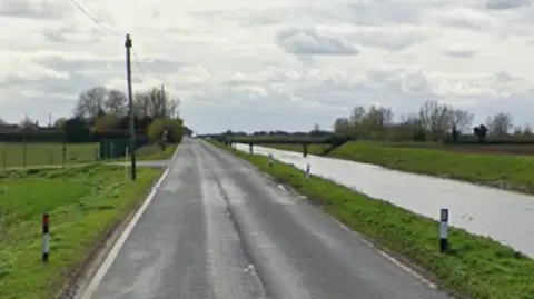 A stretch of empty road with a water filled ditch on one side.