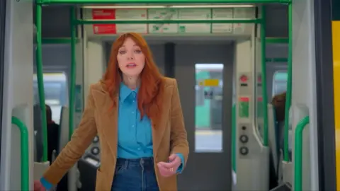 Comedy actress Diane Morgan standing in front of an open door of a train carriage