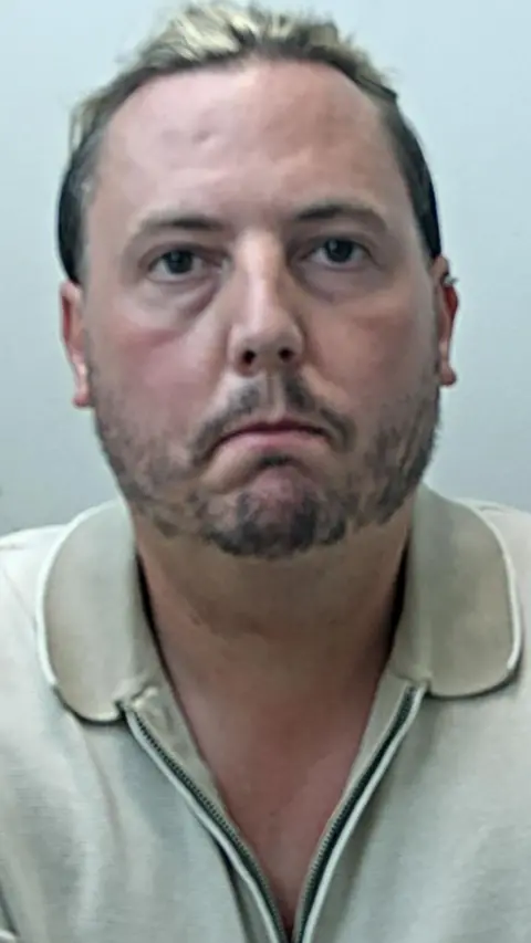 mugshot of man in police custody wearing polo top. He has a beard and long blonde hair.