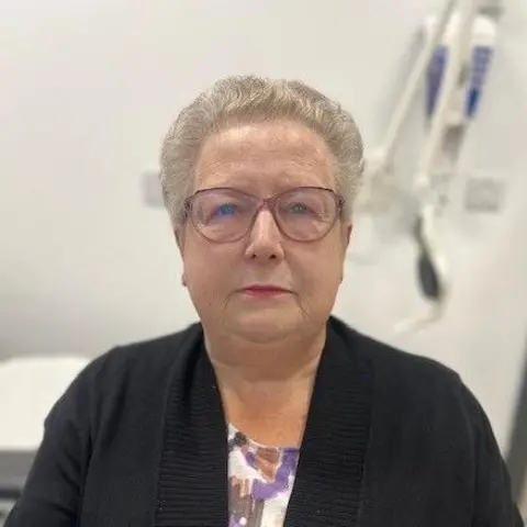 Margaret Junner, an older woman with short grey hair and glasses, wearing a dark coloured cardigan, looks at the camera.