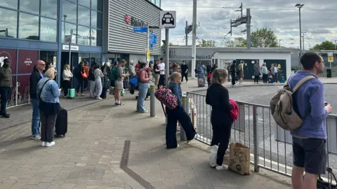 People with bags are standing outside Bristol Parkway rail station