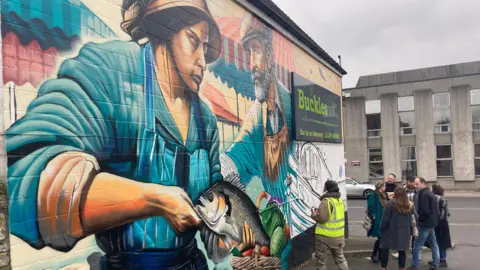 a mural showing as woman gutting a fish and an older gentleman wearing a flat cap and an apron