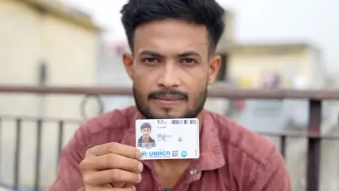 Noorul Amin, seen here holding his UNHCR card, says he lives in fear of being deported to Myanmar