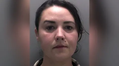 Merseyside Police Police custody image of Lisa Naylor with long dark brown tied back wearing a brown and beige shirt.