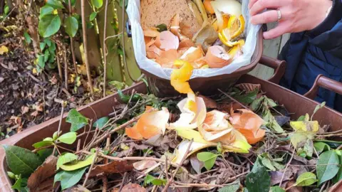 Someone scrapes some food waste into a wheelie bin full of garden waste.