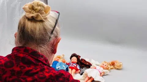 Sobell House Jay Boydon with her back to the camera. Several dolls are laid in front of her.