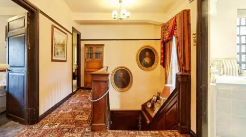 Holroyd's Estate Agents The hallway of the manor house with brown and white decor. Two Stuart-style portraits hang above the stairs