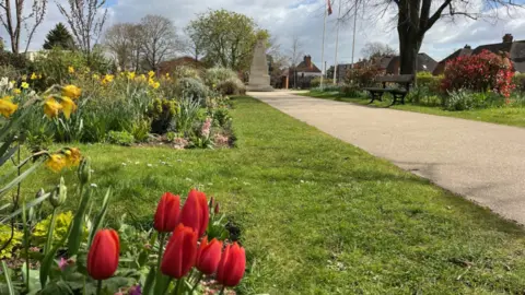 Lucy Thorne/BBC A war memorial in a park behind tulips and daffodils 