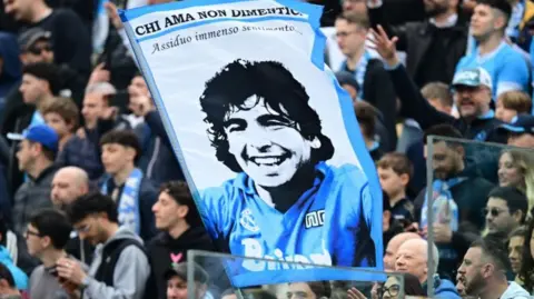 Napoli fans in the stands hold up a sign of Diego Maradona in the stands