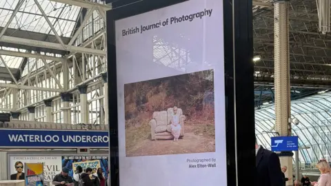 Alex Elton-Wall A digital billboard at Waterloo station in London showing a photograph of a young blonde female child sat on a beige sofa that has been dumped on a piece of land in the Forest of Dean.