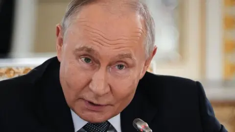 EPA Putin dressed in a dark blue suit, light blue shirt and spotted tie leans into a microphone, his eyebrows raised, at a press conference