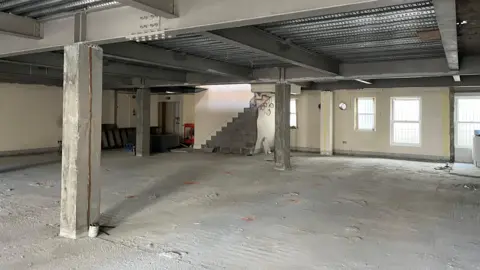 A construction site of empty building space where the flats will be. It’s very grey. 