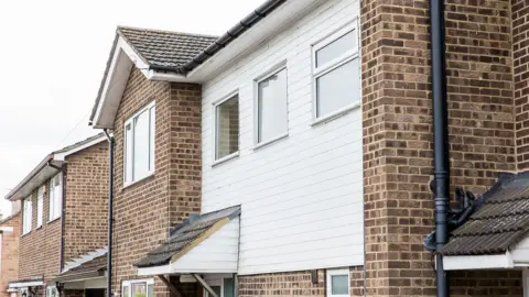 A photograph of the outside of a row of houses. They are made mostly of brick with also some white wood facias and modern double-glazed windows