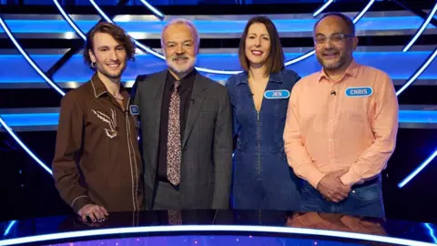 Whisper North/Rachel Joseph Photography Three contestants of ITV's Wheel of Fortune stand either side of host Graham Norton on the show's set. One man wearing a brown shirt is stood to Norton's right and a woman called Jen wearing a blue denim jump suit and a man called Chris wearing a light orange shirt stand to Norton's left.