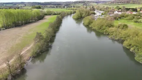 The River Thames cuts through green fields on either side in Gloucestershire.