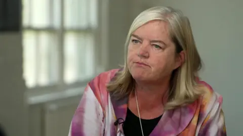 Louise Casey, Baroness Casey of Blackstock, speaking with BBC News. She is looking slightly to her right and is wearing a pink and white marbled jacket.