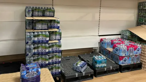 Half-empty shelves of bottled water in a supermarket.